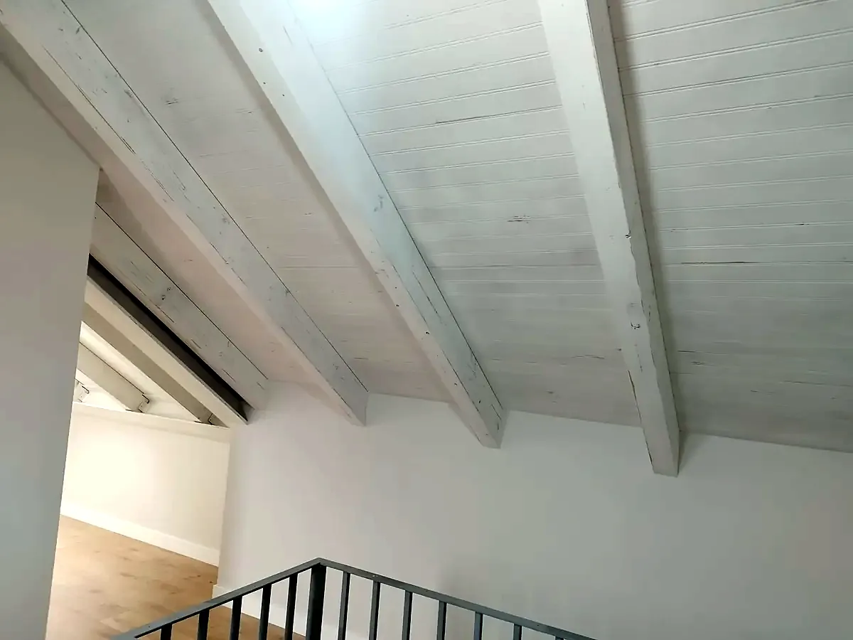 Techo de buhardilla con vigas de madera en acabado decapé